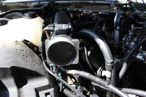 2003 Ford Crown Victoria - Close-up of a square mass-air-flow housing connected to black intake ducting and braided lines in a supercharged engine bay.
