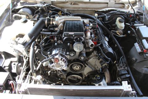2003 Ford Crown Victoria - Overhead engine bay shot showing a supercharger, alternator, belt pulleys and brake master cylinder reservoir.