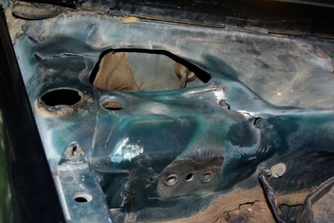 1995 Ford Bronco - The firewall of a vehicle shows signs of wear and tear, with several openings and damaged areas.