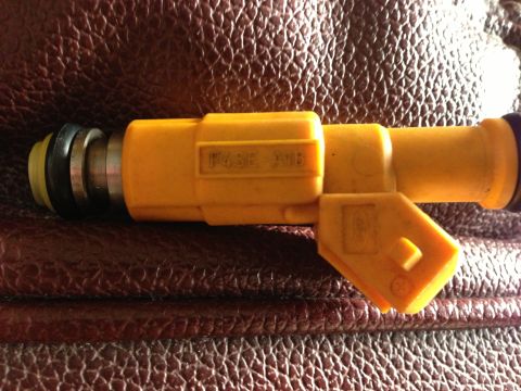 1989 Ford Bronco - A single yellow fuel injector is shown against a textured brown background.