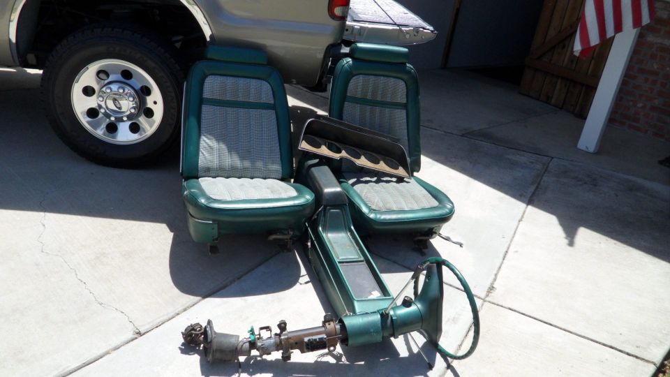 Green car seats and a steering column assembly on a concrete surface next to a truck tire