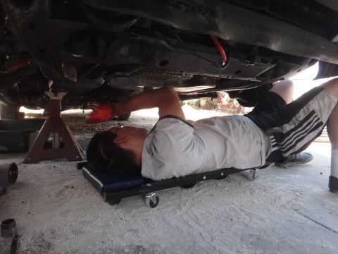 1993 Ford Taurus - A person lies on a creeper, working on the underside of a vehicle supported by jack stands.