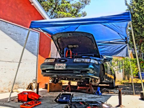 1993 Ford Taurus - A 1993 Ford Taurus SHO is raised on jack stands for maintenance under a blue canopy.