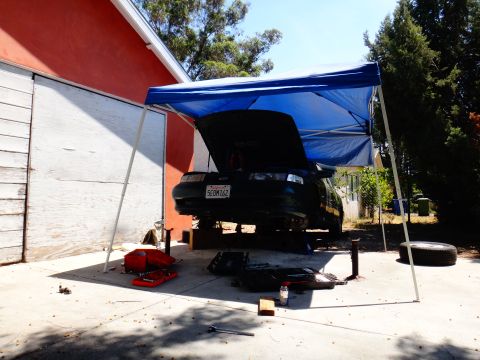 1993 Ford Taurus - Car repair in progress under a canopy. Tools and spare tire are visible nearby.