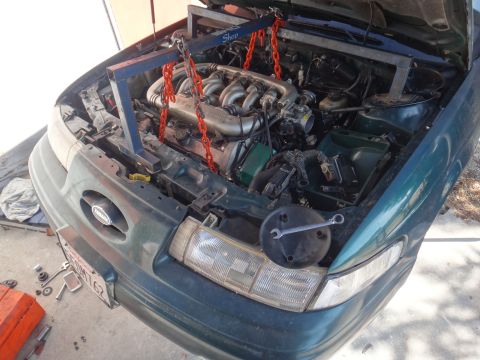 1993 Ford Taurus - Engine bay of a 1993 Ford Taurus with the engine supported by an engine hoist.