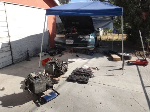 1993 Ford Taurus - A green 1993 Ford Taurus is undergoing engine work, with the hood up and engine components laid out on the driveway.