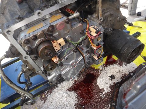 1993 Ford Taurus - Close-up of an automatic transmission valve body, showing solenoids, wiring, and spilled transmission fluid mixed with debris.