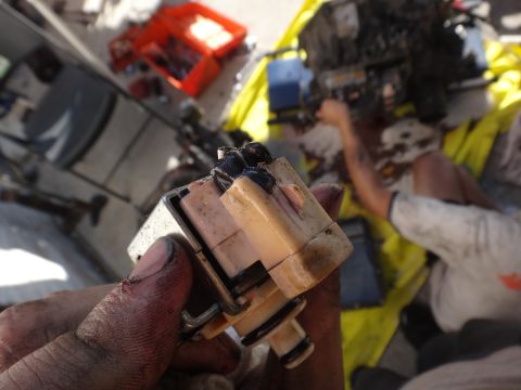1993 Ford Taurus - Close-up of a greasy electrical component being held, with a blurred background of a person working on an engine.