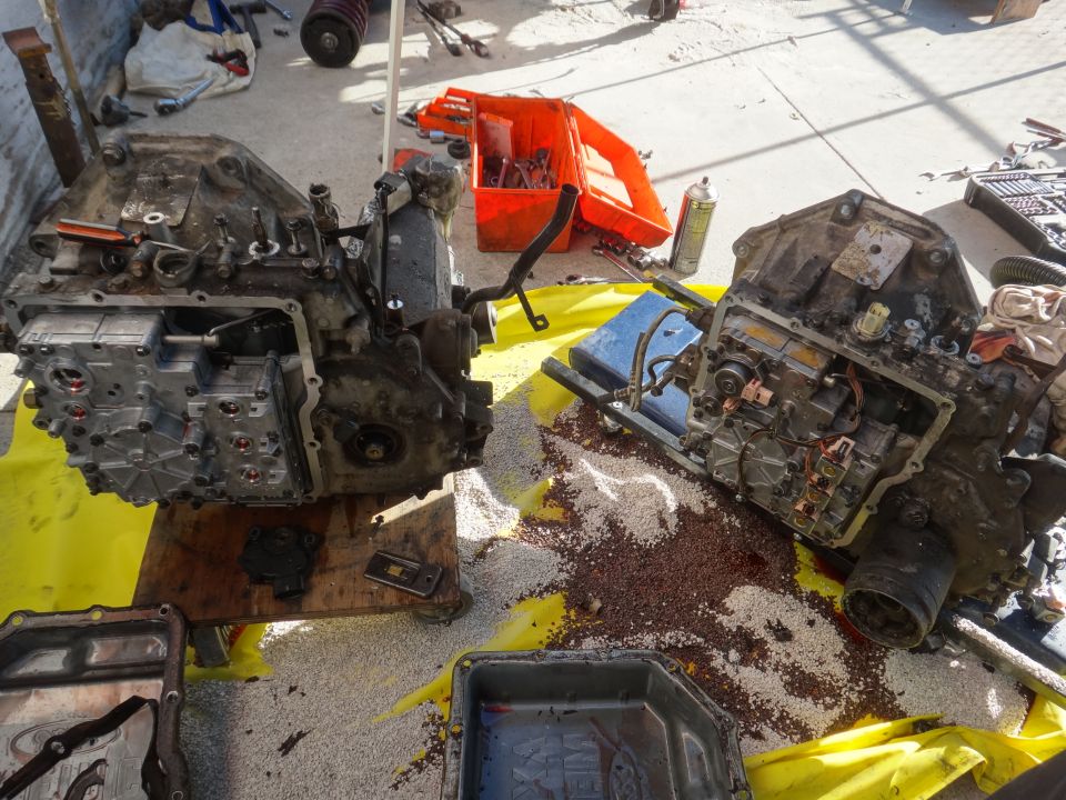 Two disassembled automatic transmissions on a yellow tarp with tools and parts scattered around