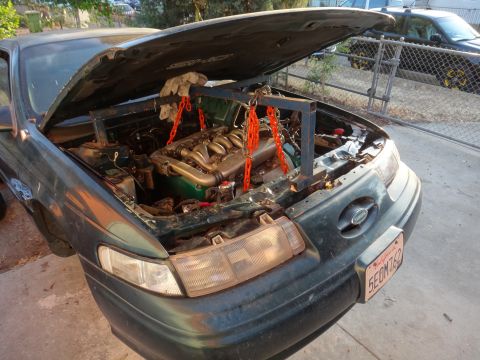 1993 Ford Taurus - Engine removal in progress on a 1993 Ford Taurus, using a support frame and chains.