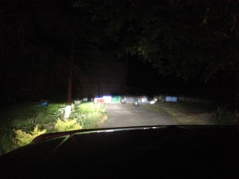 1992 Ford F-150 - The bright headlights cut through the darkness, illuminating a driveway with some distant vehicles visible.
