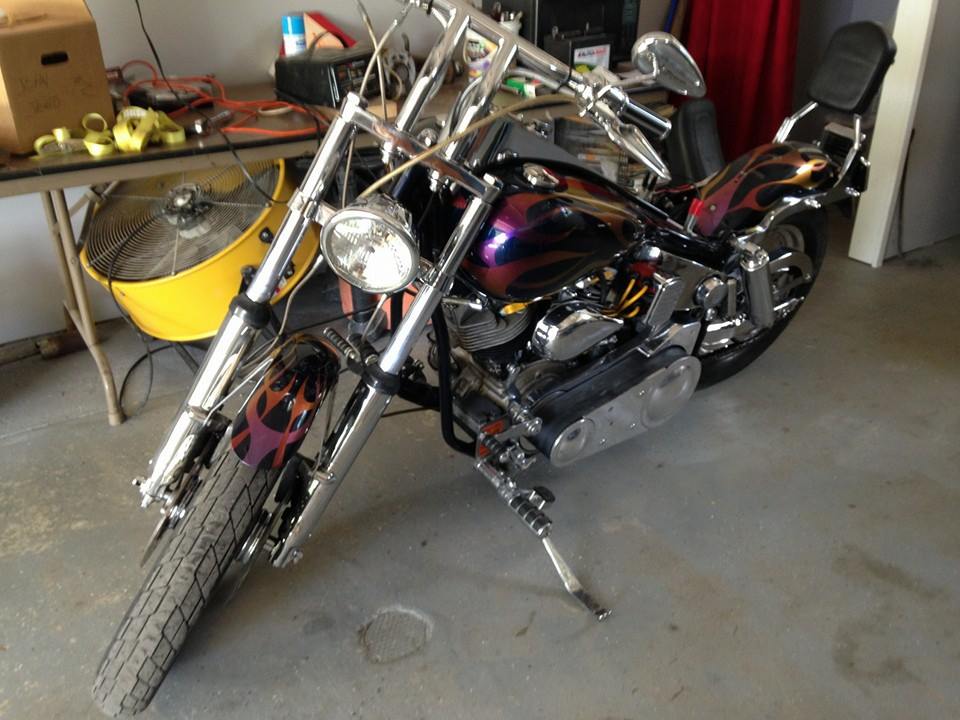 Chopper-style motorcycle with purple and orange flames on the tank and fenders, parked indoors