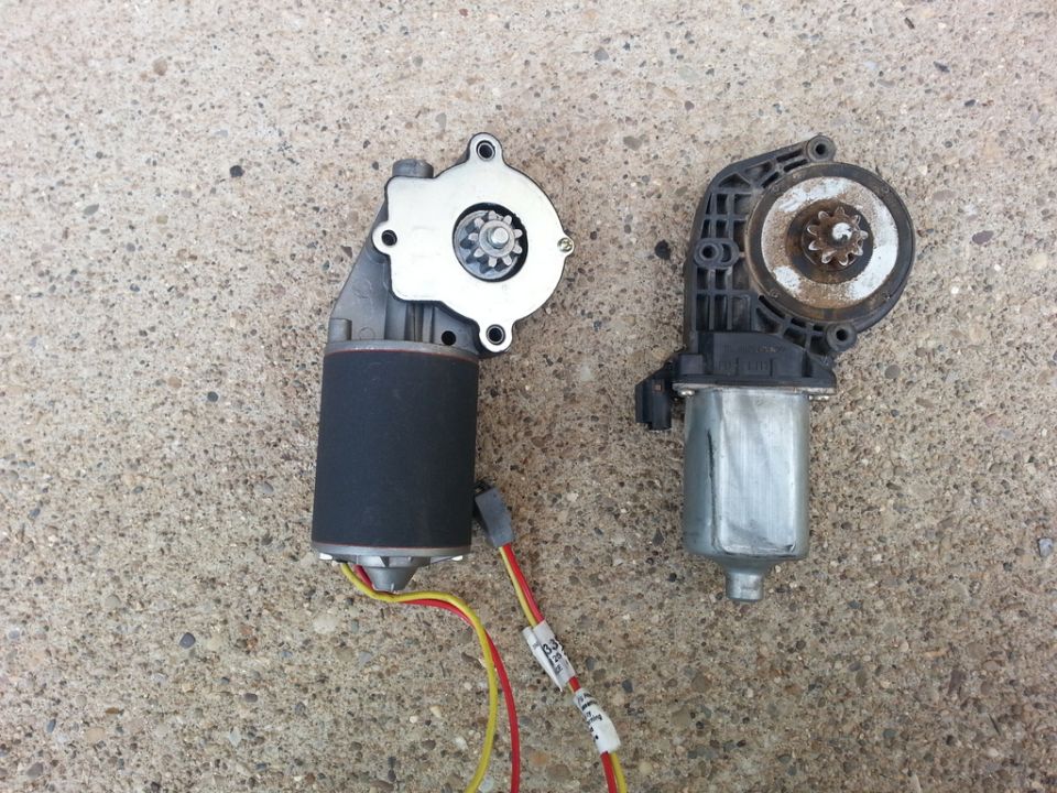New black window motor with wiring next to a rusty used window motor on concrete