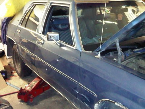 1981 Ford Crown Victoria - The vehicle is being worked on, with the hood open and a jack supporting the front.