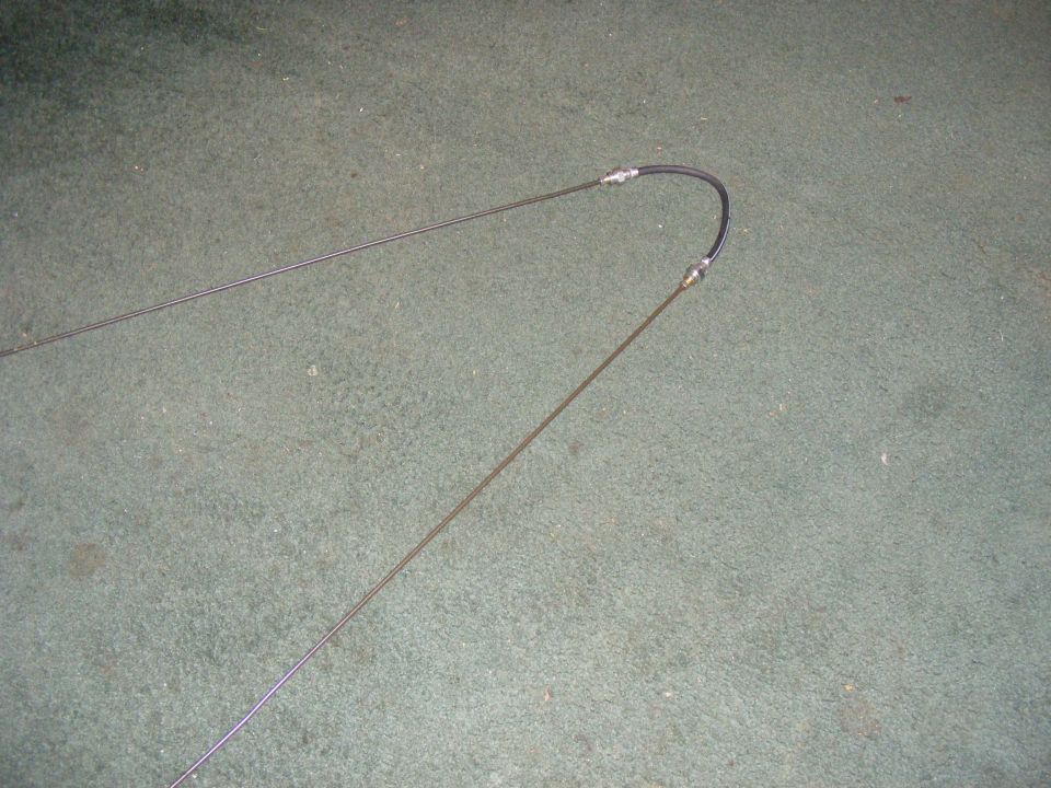 Two throttle cables, one with a black protective sleeve, laid out on a carpeted surface