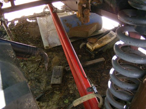 Close-up of a red suspension component, large coil spring, and various debris under a vehicle