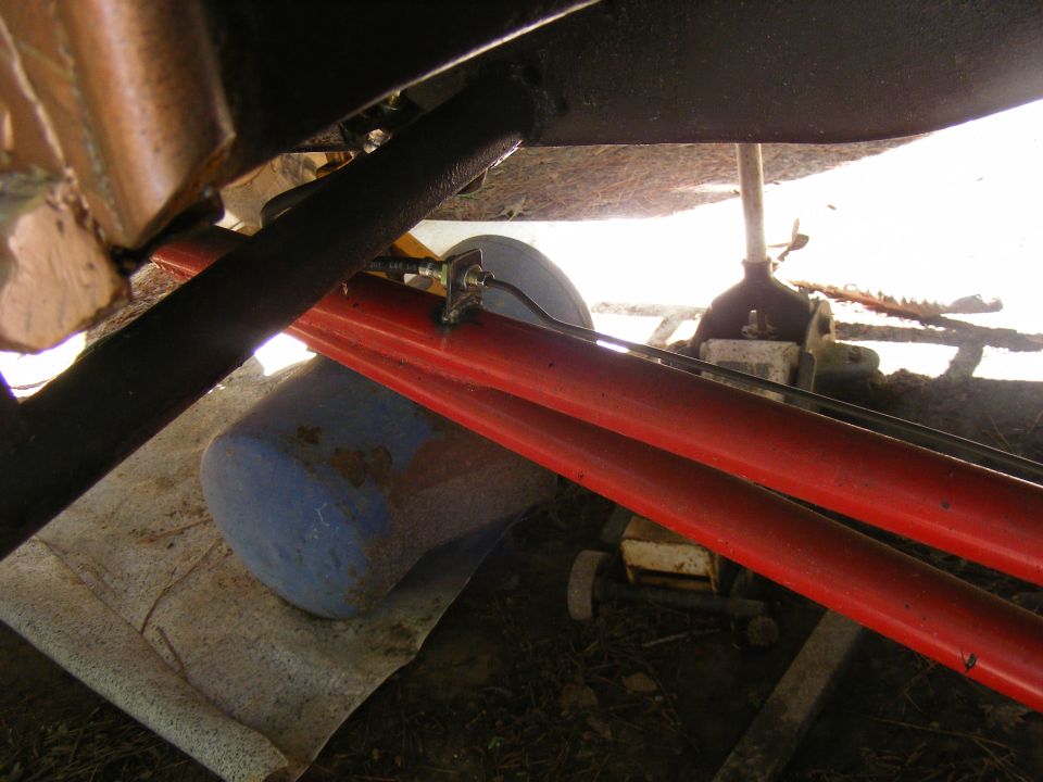 Undercarriage of a vehicle with bright red suspension arms and black frame components, supported by a jack