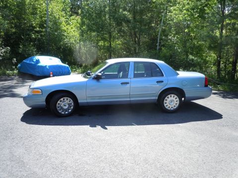 2001 Ford Crown Victoria - Side view of a light blue 2001 Ford Crown Victoria sedan parked outdoors with trees in the background. A second vehicle is covered by a blu…