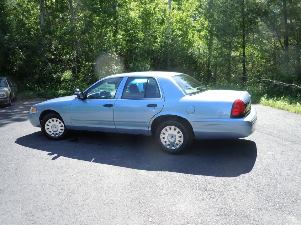 2001 Ford Crown Victoria, light blue, parked on asphalt with trees in background