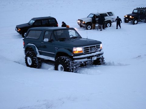 1996 Ford Bronco - Several off-road vehicles navigate a snowy landscape, with one Bronco in the foreground making tracks.