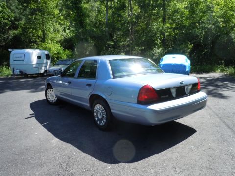2001 Ford Crown Victoria - A light blue sedan is parked outdoors next to a trailer and another covered object.