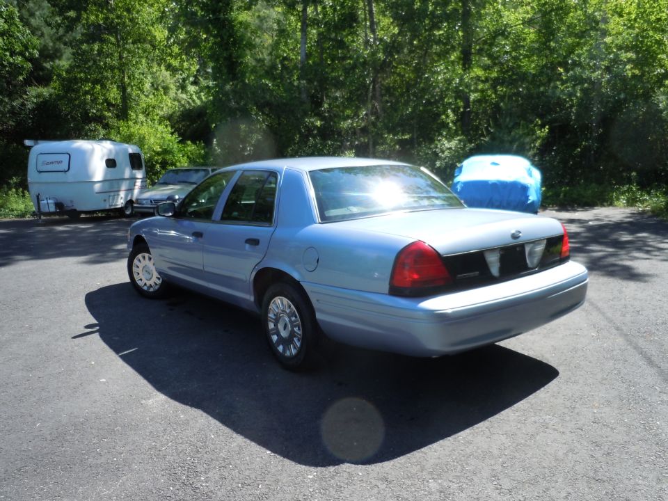 Light blue sedan parked on asphalt, with a trailer and a blue-covered object behind it