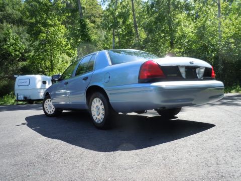 2001 Ford Crown Victoria - A light blue 2001 Ford Crown Victoria sedan is parked on an asphalt surface with a small white trailer behind it.