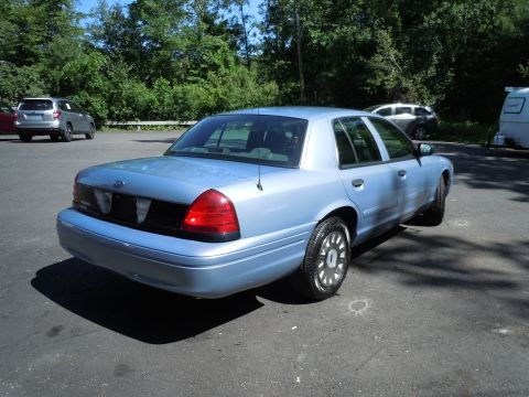 2001 Ford Crown Victoria - Light blue 2001 Ford Crown Victoria seen from the rear quarter angle with other vehicles in the background.