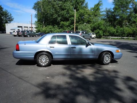 2001 Ford Crown Victoria - A light blue sedan is parked in an asphalt lot with trees and other vehicles visible.