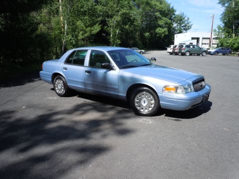 2001 Ford Crown Victoria - A light blue sedan is parked on an asphalt lot with trees in the background.