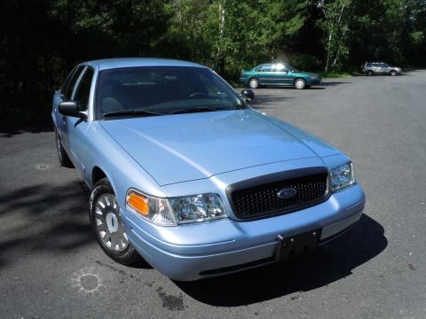 2001 Ford Crown Victoria - A light blue 2001 Ford Crown Victoria is parked in a lot with other vehicles in the background.
