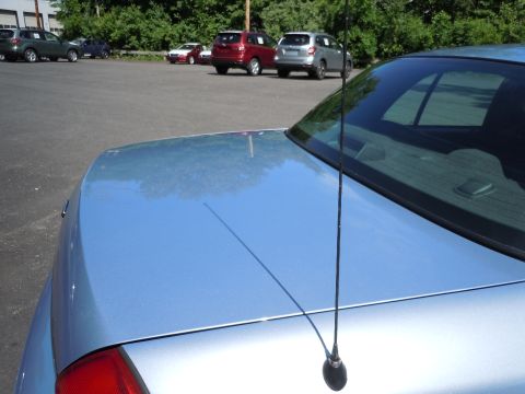 2001 Ford Crown Victoria - A light blue sedan's trunk and rear window are visible, with other vehicles parked in a lot behind it.
