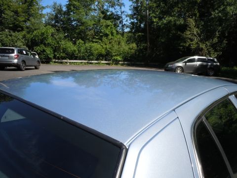 2001 Ford Crown Victoria - A light blue car's roof reflects the sky and trees, with two other vehicles parked nearby.