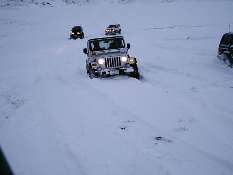 1996 Ford Bronco - Multiple Jeep Wranglers navigate a snowy landscape, kicking up snow as they drive.