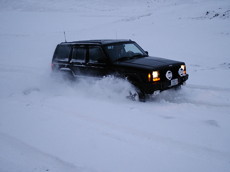 Dark Jeep Cherokee XJ SUV driving through deep snow, front 3/4 view