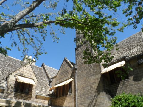 1971 Ford Ranchero - A stone building with multiple gabled roofs and awnings is partially obscured by tree branches against a clear blue sky.