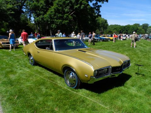 1971 Ford Ranchero - Gold 1970 Oldsmobile 442 coupe on display at a car show with other vehicles in the background.