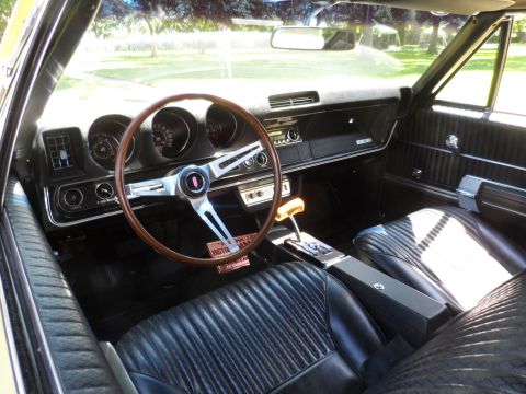 1971 Ford Ranchero - The interior of a classic car shows a wood steering wheel and black seats.