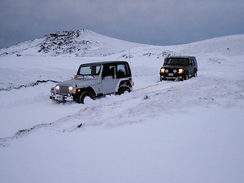 1996 Ford Bronco - Two Jeeps struggle through deep snow, one pulling the other with a tow strap.