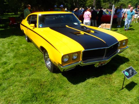 1971 Ford Ranchero - A bright yellow muscle car with black racing stripes is displayed on a grassy lawn at an outdoor event.