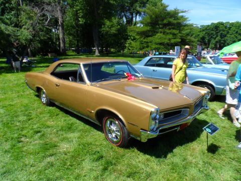 1971 Ford Ranchero - A gold 1966 Pontiac GTO is displayed at an outdoor car show with other vehicles present.