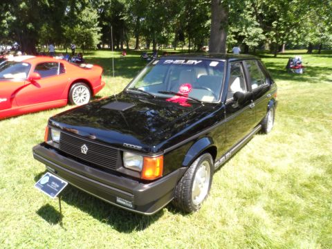 1971 Ford Ranchero - A black Dodge Omni Shelby is displayed on a grassy field, with a red sports car visible to its left.