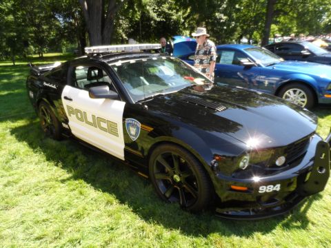 1971 Ford Ranchero - A black and white police car is parked on a grassy lawn at an outdoor event, with other vehicles visible in the background.
