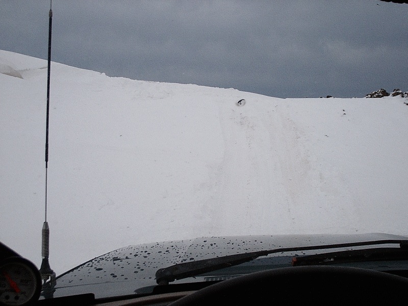 Driver's-eye view over vehicle hood toward snowy hill with tire tracks