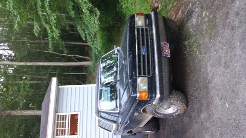 1991 Ford Bronco - This black Ford Bronco is parked in a driveway next to a house with trees in the background.