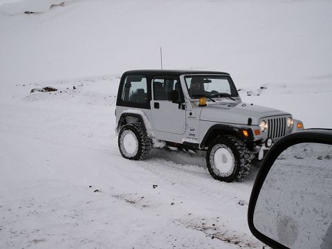 1996 Ford Bronco - A Jeep Wrangler navigates a snowy landscape, with its tires kicking up snow.