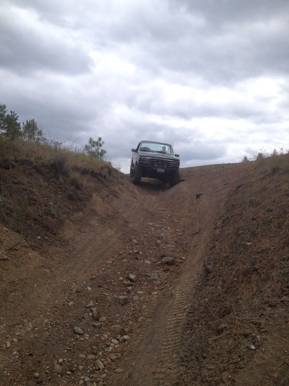 Black pickup truck driving up a dirt hill under a cloudy sky