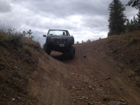 2005 Jeep Wrangler - A lifted truck navigates a steep, off-road trail on a cloudy day.