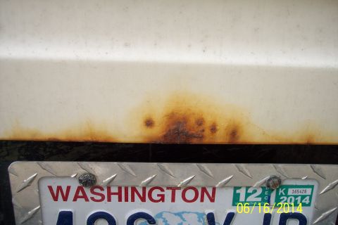 1990 Ford Bronco - The lower portion of a vehicle's body panel shows significant rust damage near the license plate.