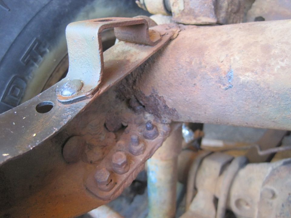 Close-up of heavily rusted vehicle frame and suspension parts, with a tire visible on the left